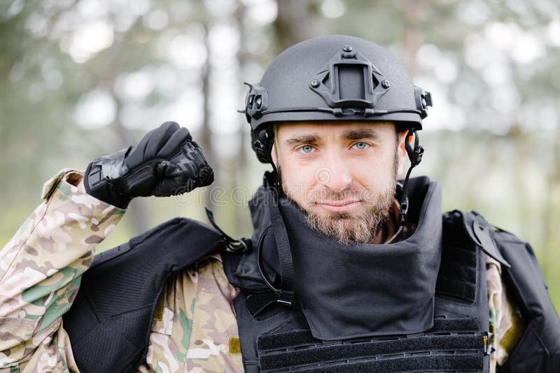 Un hombre con uniforme militar y chaleco antibalas se sienta en el bosque  cerca de un detector de metales.
