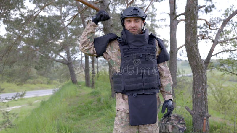 Un hombre con uniforme militar y chaleco antibalas trabaja en el bosque con  un detector de metales.