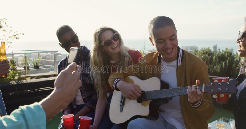Un joven tocando guitarra en la azotea con sus amigos metrajes