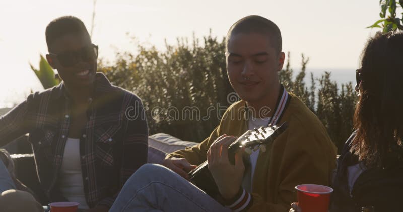 Un joven tocando guitarra en la azotea con sus amigos metrajes