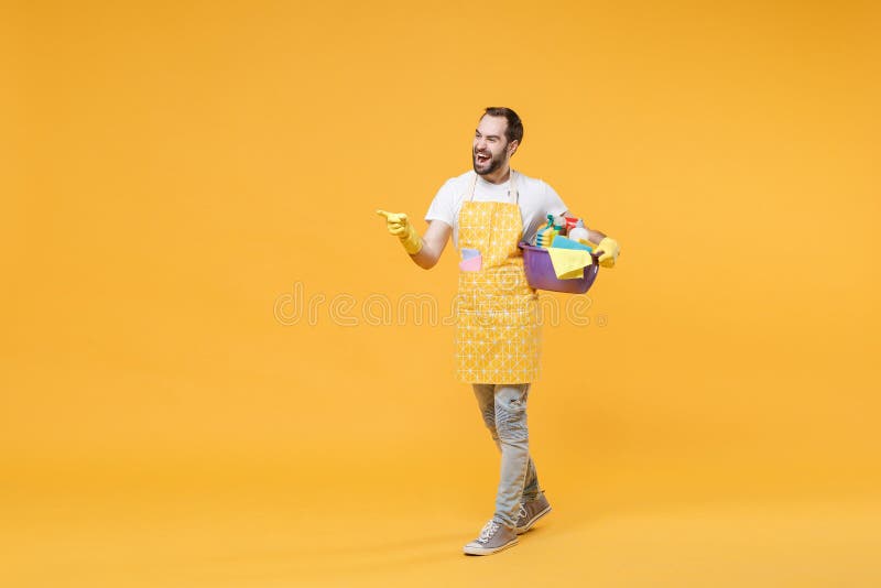 Un joven y alegre ama de casa en guantes de goma de delantal sostienen botellas detergentes lavadoras lavadoras de cuencas haciend imagenes de archivo