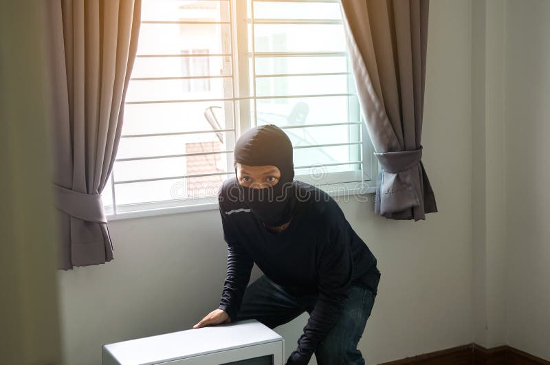 Un ladrón del hombre en máscara negra que roba la TV de la casa fotos de archivo libres de regalías Un ladrón del hombre en máscara negra que roba la TV de la casa fotos de archivo libres de regalías