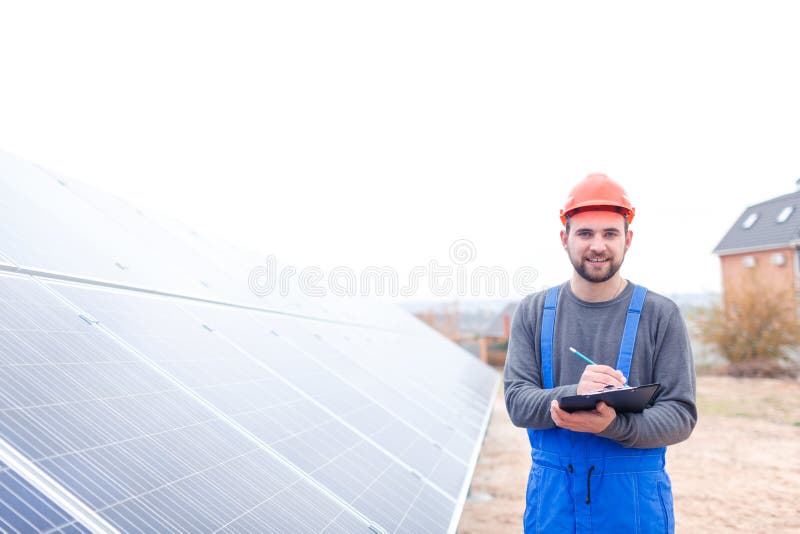 Un lavoratore solare della stazione sta vicino al pannello di batteria solare e scrive qualcosa in un blocco note all'aperto fotografie stock Un lavoratore solare della stazione sta vicino al pannello di batteria solare e scrive qualcosa in un blocco note all'aperto fotografie stock