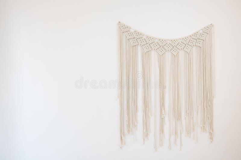 A macrame the art of knotting cord or string in patterns hanging on white cement wall for home and wedding decoration with copy space. A macrame the art of knotting cord or string in patterns hanging on white cement wall for home and wedding decoration with copy space