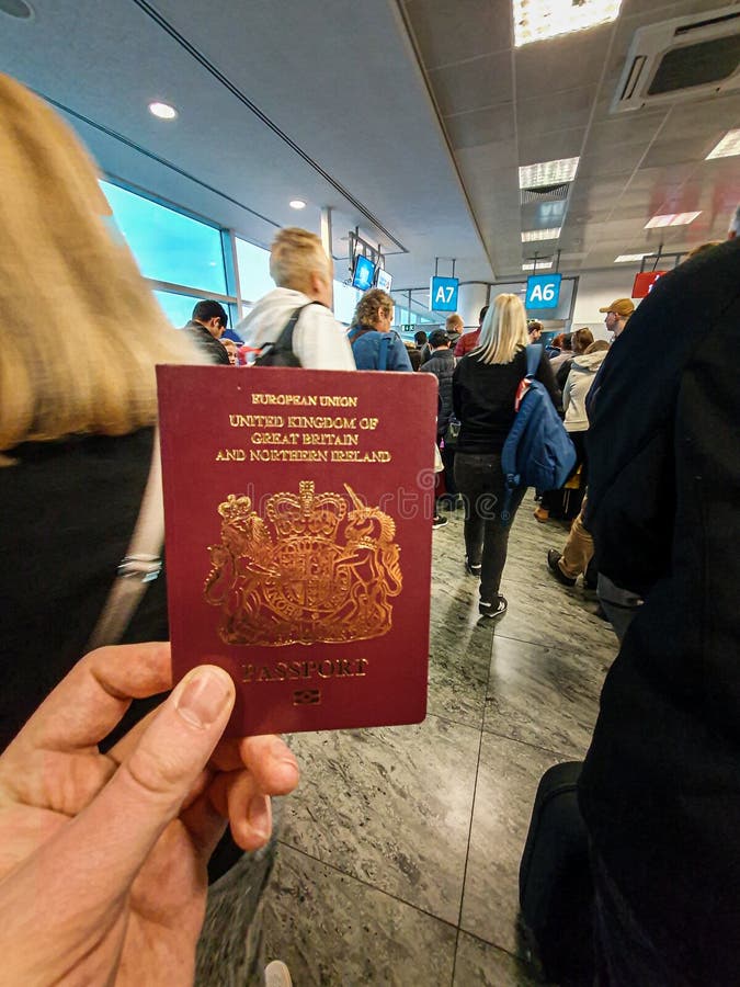 Un maschio bianco tiene il suo passaporto britannico rosso in sua mano in mezzo ad un terminale ammucchiato di partenza immagini stock Un maschio bianco tiene il suo passaporto britannico rosso in sua mano in mezzo ad un terminale ammucchiato di partenza immagini stock