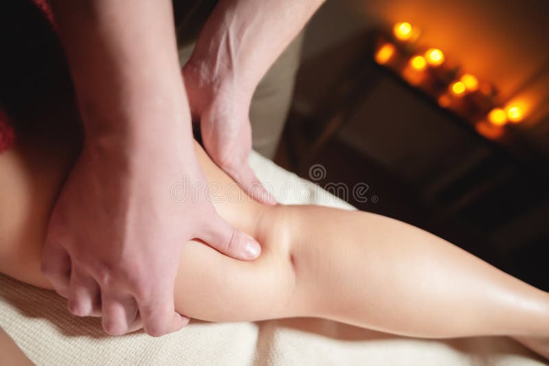 A men masseur does a massage of the thigh and lower leg to a women client in a dark room of the massage room. A men masseur does a massage of the thigh and lower leg to a women client in a dark room of the massage room.