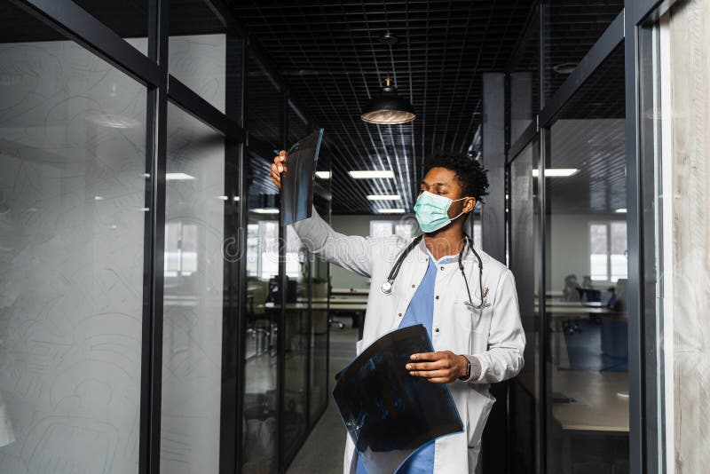 Un medico africano esamina gli esperimenti in una clinica medica. uno studente di colore con maschera medica sta studiando e guard immagini stock libere da diritti