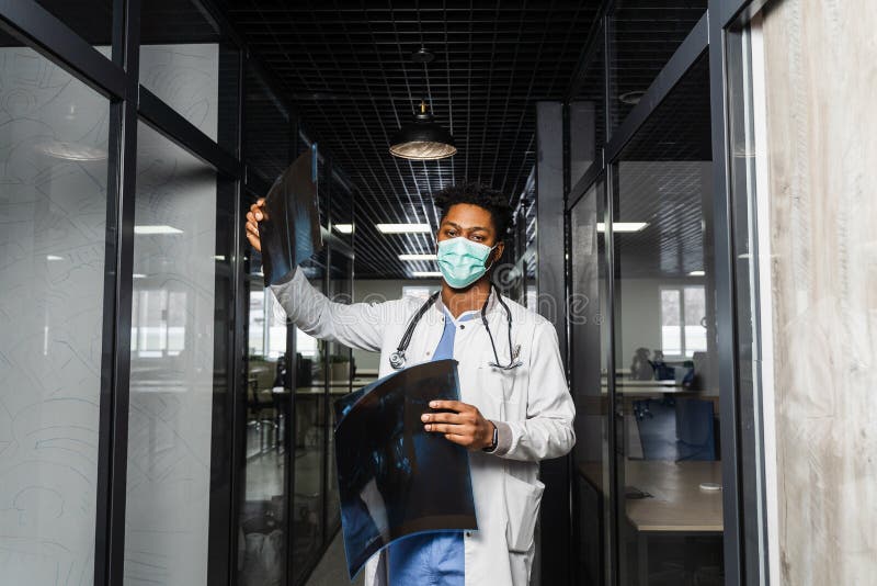 Un medico africano esamina gli esperimenti in una clinica medica. uno studente di colore con maschera medica sta studiando e guard fotografia stock
