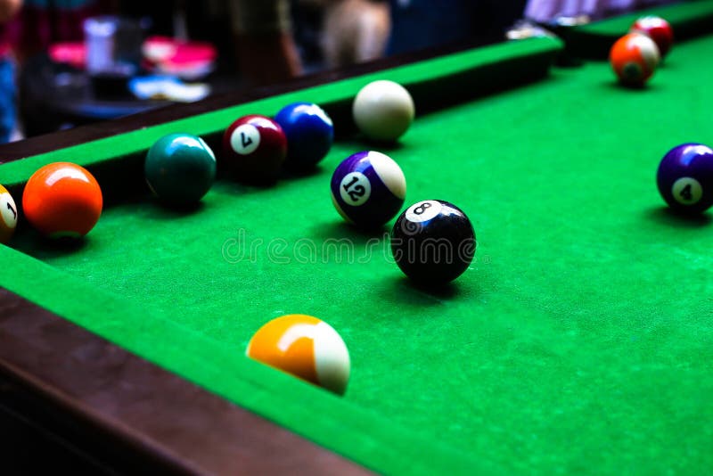 Colourful billiard balls on the green cloth table in the pub full of billiard players. Colourful billiard balls on the green cloth table in the pub full of billiard players