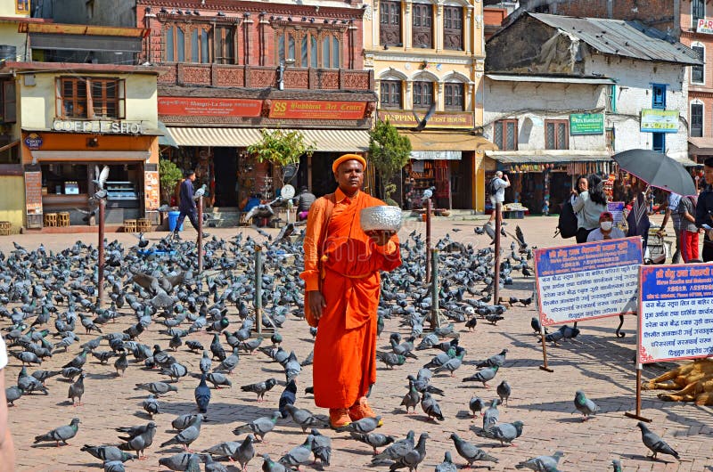 Un moine Buddhish dans des vêtements oranges lumineux s'établissant à la place de Bouddha Stupa, Népal photographie stock libre de droits