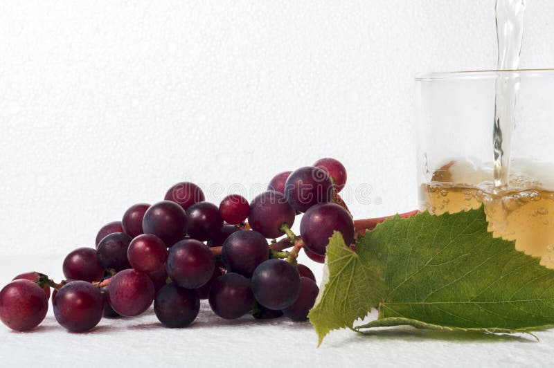 Un montón de uvas con hojas verdes sobre un fondo blanco. Un vaso de zumo de uva con un chorro de zumo que sale de arriba imagen de archivo libre de regalías Un montón de uvas con hojas verdes sobre un fondo blanco. Un vaso de zumo de uva con un chorro de zumo que sale de arriba imagen de archivo libre de regalías