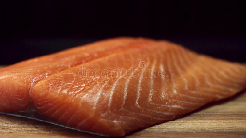 Un morceau de poissons frais, crus, rouges sur une planche à découper brune en bois, d'isolement sur le fond noir Beau filet saum