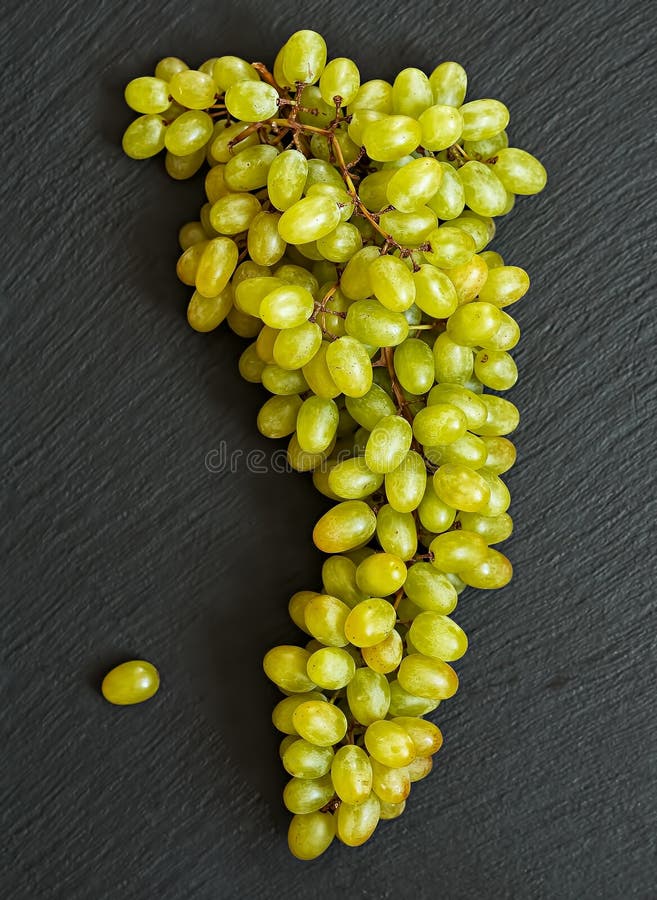 A bunch of ripe green grapes is located on a black stone background. A bunch of ripe green grapes is located on a black stone background.