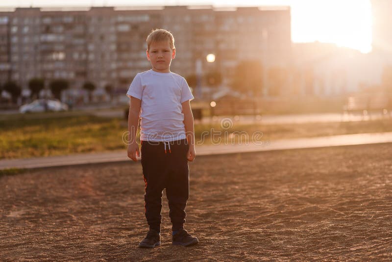 Un muchacho contrariedad en una camiseta blanca en miradas completas del crecimiento en la cámara en la luz de la puesta del sol