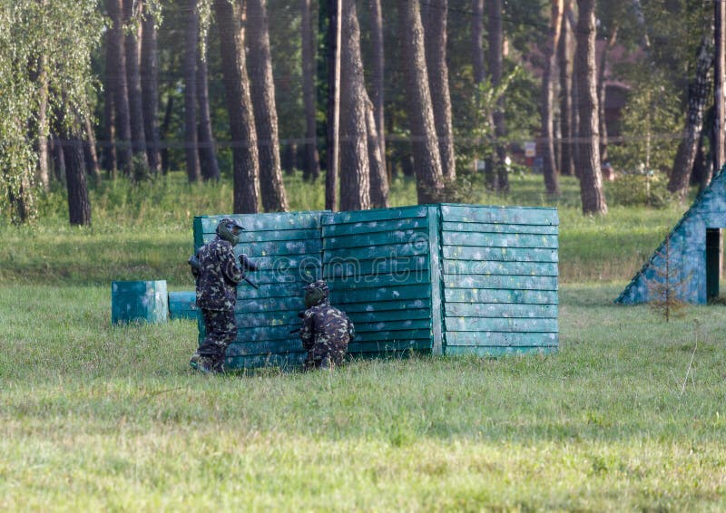 Un muchacho está jugando Paintball en el campo dos equipos de jugadores de Paintball en forma del camuflaje con las máscaras, cas fotografía de archivo libre de regalías Un muchacho está jugando Paintball en el campo dos equipos de jugadores de Paintball en forma del camuflaje con las máscaras, cas fotografía de archivo libre de regalías