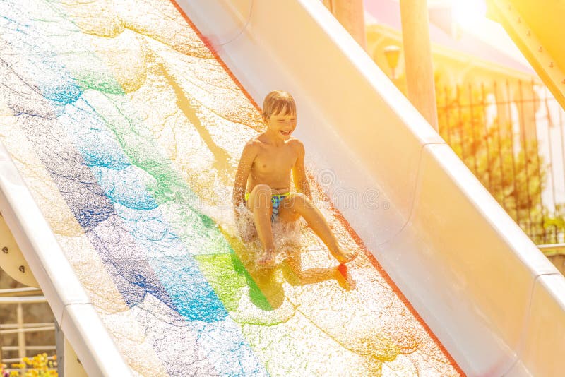 Un muchacho feliz en el tobogán acuático en una piscina que se divierte durante vacaciones de verano en aguamarina hermosa parque fotos de archivo Un muchacho feliz en el tobogán acuático en una piscina que se divierte durante vacaciones de verano en aguamarina hermosa parque fotos de archivo