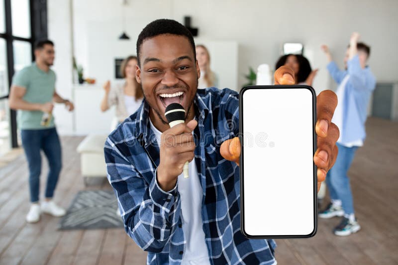 Un negro excitado mostrando una pantalla blanca vacía de un smartphone con micrófono imagen de archivo libre de regalías