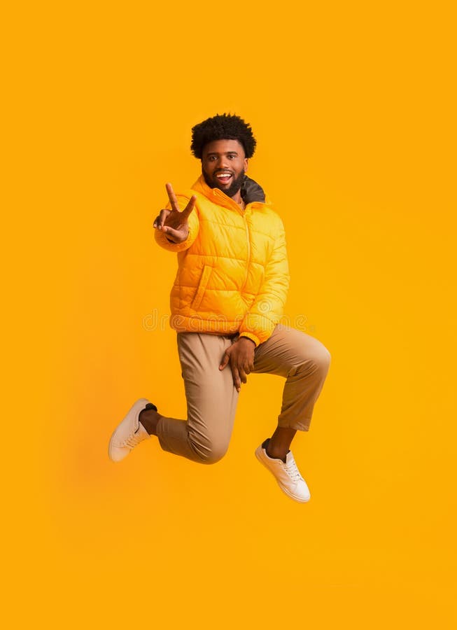 Positive winter black man greeting with peace gesture while jumping in the air. Positive winter black man greeting with peace gesture while jumping in the air