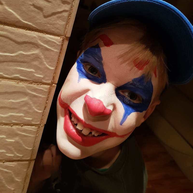  Un Niño Alegre Con Una Máscara De Payaso Pintada En La Cara Asoma a La Esquina Pintura Corporal Y Maquillaje Para Un Carnaval Esc Foto de archivo
