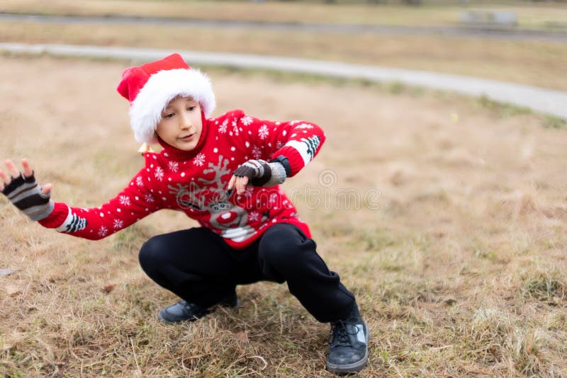 Un Niño Con Un Cálido Jersey Navidad Con Un Venado De Nuevos Años Y Con Un Sombrero De Santa Que Hace Diferentes Poses De Yoga Foto de archivo - Imagen de