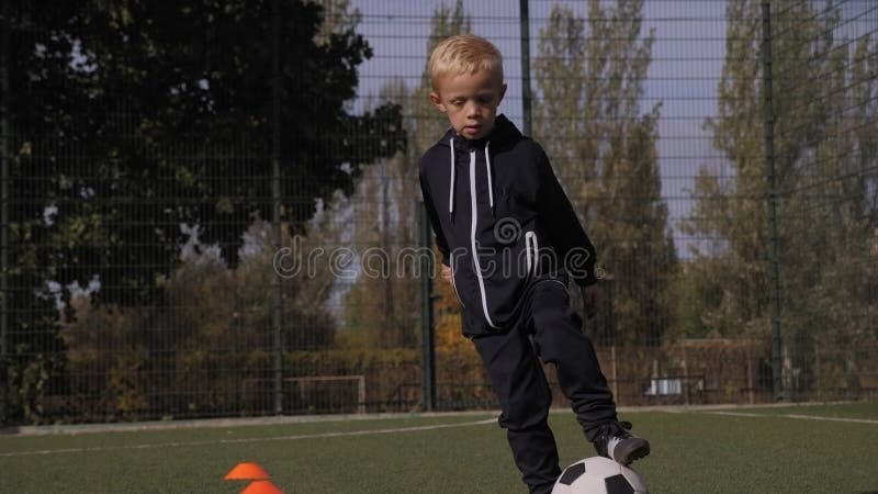 Un niñito entrena en el campo de fútbol entre conos anaranjados. metrajes
