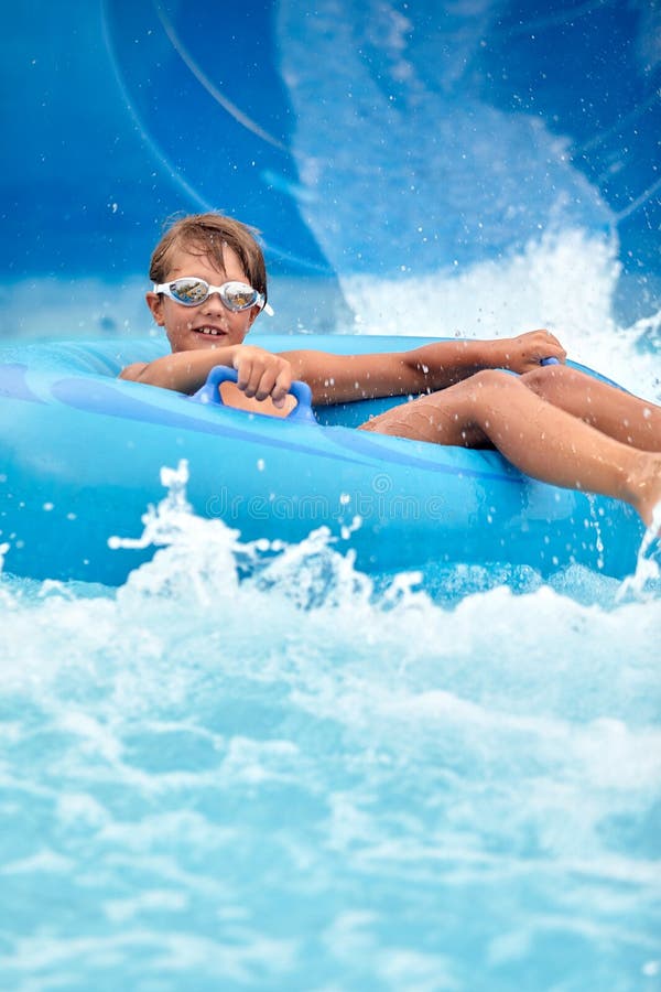 Un niño alegre desciende sobre un círculo inflable desde el tobogán de agua en el parque acuático los niños atracciones en imagenes de archivo