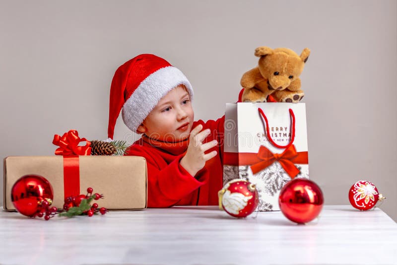 Un niño con traje de santa claus mirando regalos de navidad. retrato de cierre sobre fondo beige fotos de archivo libres de regalías