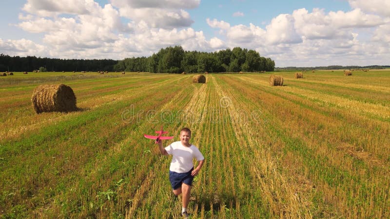 Un niño corre alegremente con un avión en la mano a través de un campo cortado. almacen de video