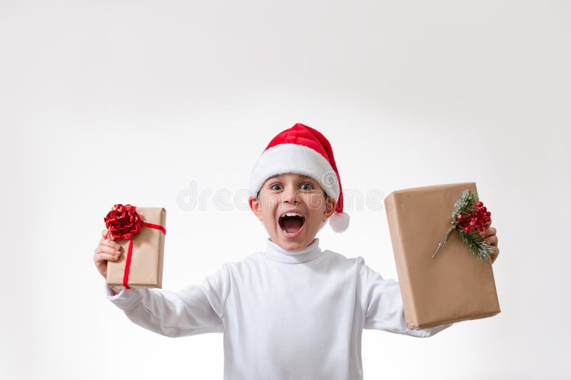 Un niño en gritos rojos de un sombrero de santa mientras que ostenta regalos de Navidad. Concepto de Navidad imagen de archivo libre de regalías