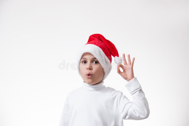 Un niño en un sombrero rojo de santa muestra un gesto de fotos de archivo
