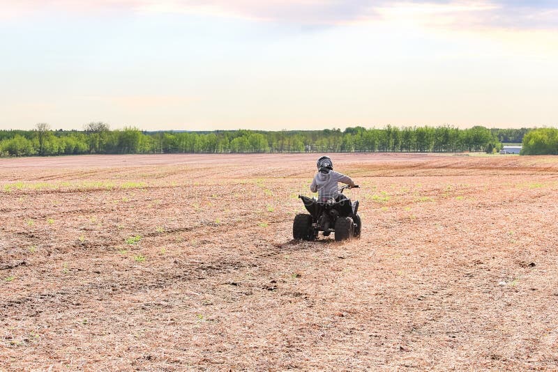 Un niño joven quading lejos en un campo abierto de la primavera imagen de archivo Un niño joven quading lejos en un campo abierto de la primavera imagen de archivo