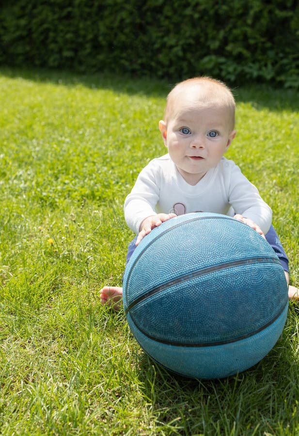 Un niño pequeño con un gran baloncesto sentado sobre el césped verde en un día soleado imágenes de archivo libres de regalías