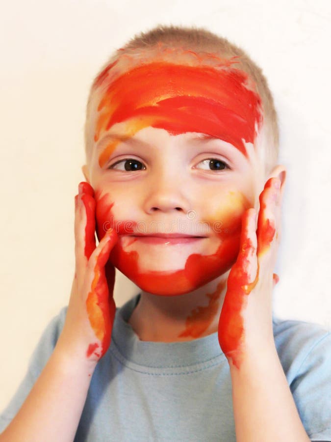 Un niño pequeño con la cara y las manos manchadas con las pinturas coloreadas foto de archivo Un niño pequeño con la cara y las manos manchadas con las pinturas coloreadas foto de archivo