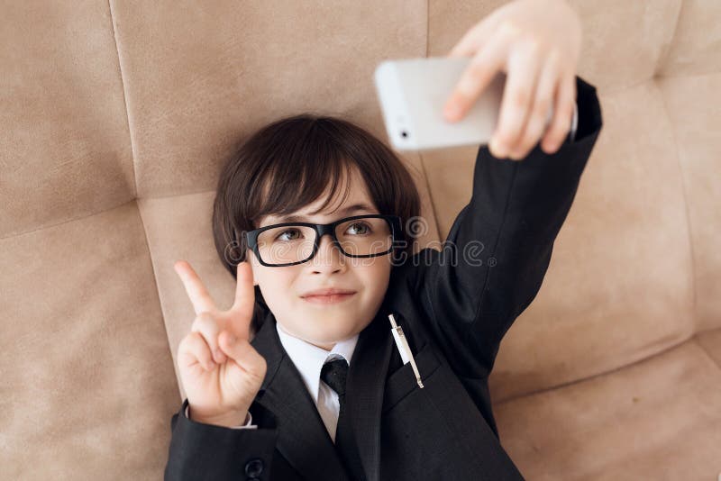 Un niño pequeño en vidrios y traje se presenta como hombre de negocios El muchacho oscuro-cabelludo juega a un hombre rico foto de archivo Un niño pequeño en vidrios y traje se presenta como hombre de negocios El muchacho oscuro-cabelludo juega a un hombre rico foto de archivo