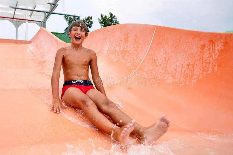Un niño se desliza por un tobogán de agua naranja en el parque acuático y unas vacaciones de ánimo alegres para los niños fotografía de archivo libre de regalías