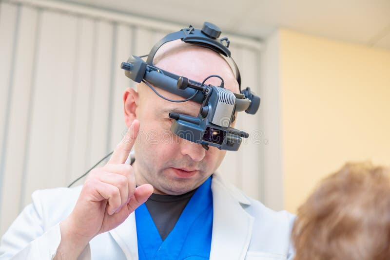 Un oftalmologo maschile controlla la vista di una donna adulta con oftalmoscopio binoculare immagini stock