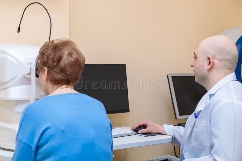 Un oftalmologo maschio controlla la vista di una donna adulta usando un dispositivo moderno fotografie stock