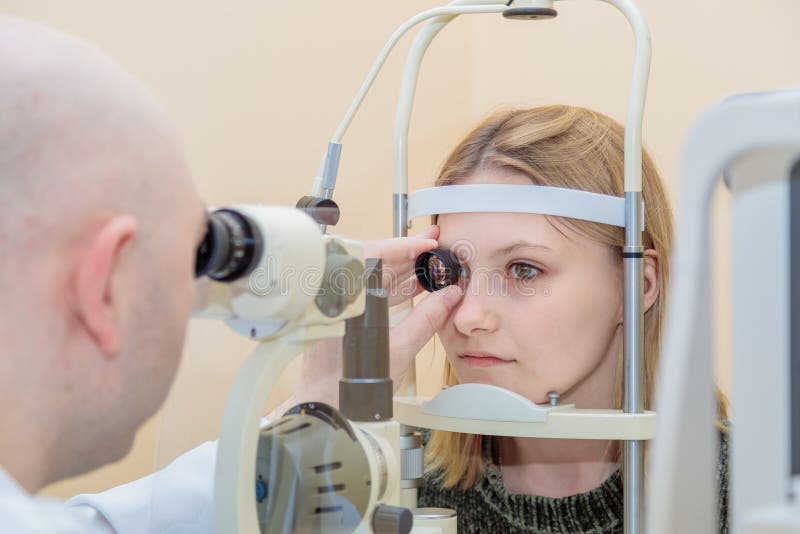 Un oftalmologo maschio controlla la vista di una ragazza usando un dispositivo moderno con una trave leggera immagini stock