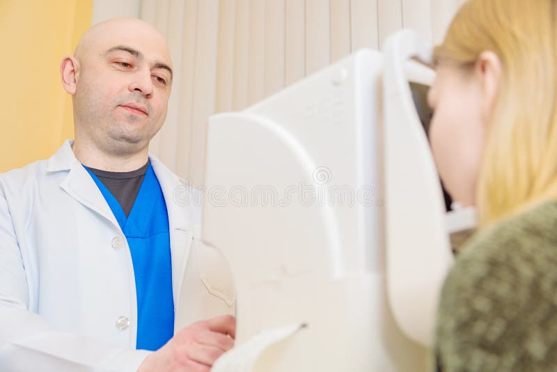 Un oftalmologo maschio controlla la vista di una ragazza usando un moderno tester visivo fotografie stock