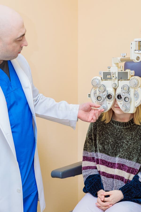 Un oftalmologo maschio controlla la vista di una ragazza usando un phoropher. trattamento visivo immagine stock
