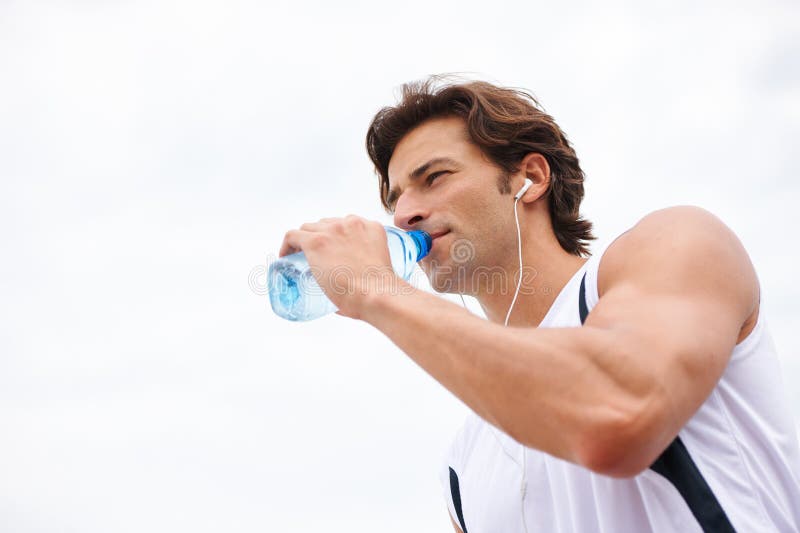 Un om care bea apă în pauză de la exerciții însetate și ascultând muzică podcast sau cântec pe fugă. Sportiv masculin royalty free stock photo