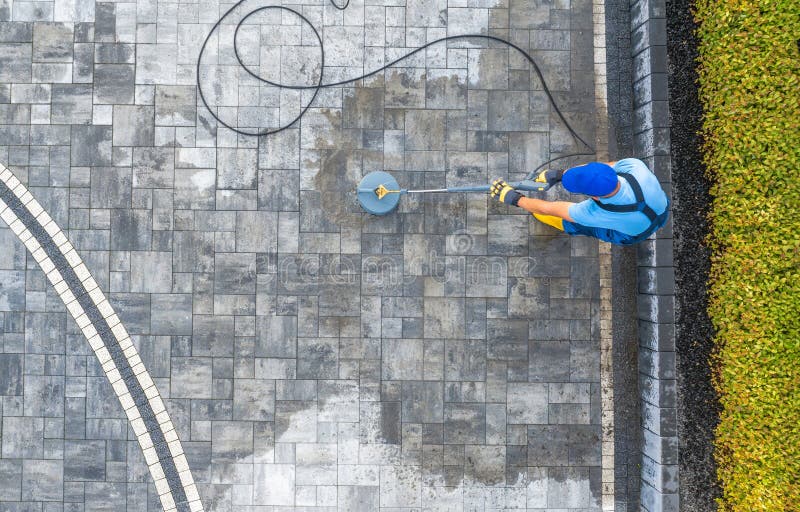 Un operaio pulisce la superficie del patio all'aperto con una lavatrice a pressione al sole fotografia stock libera da diritti