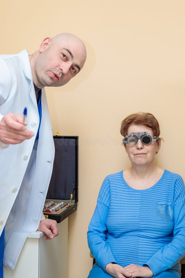 Un optometrista maschio controlla la vista di una donna adulta con una cornice di prova fotografia stock libera da diritti