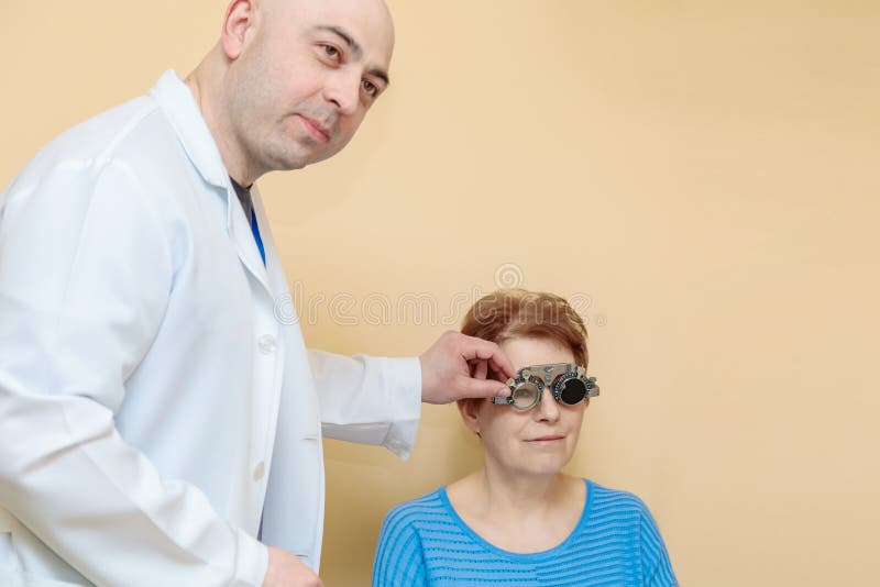 Un optometrista maschio controlla la vista di una donna adulta con una cornice di prova fotografia stock