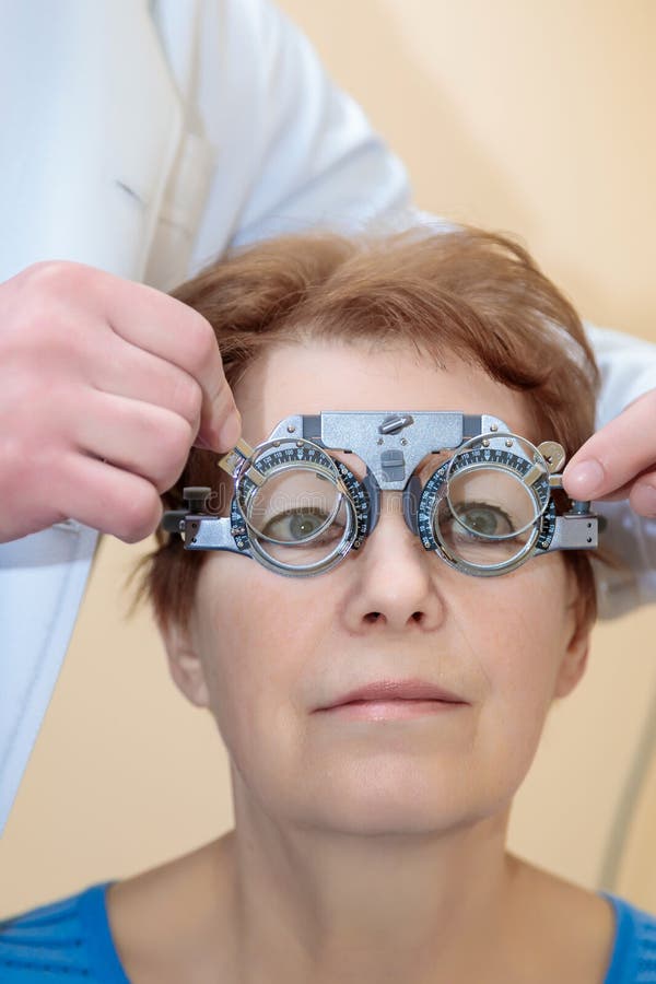 Un optometrista maschio controlla la vista di una donna adulta con una cornice di prova fotografie stock