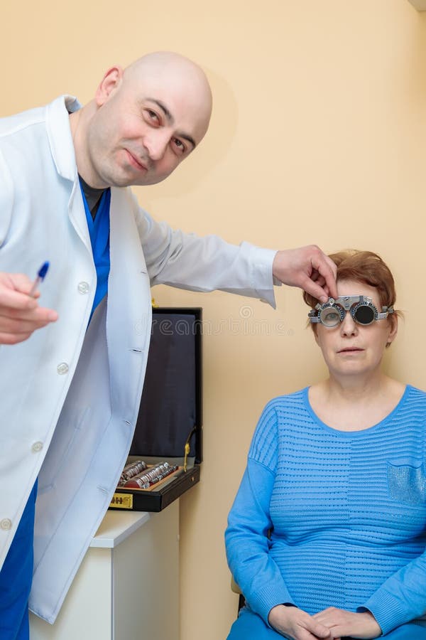 Un optometrista maschio controlla la vista di una donna adulta con una cornice di prova fotografia stock