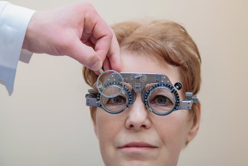 Un optometrista maschio controlla la vista di una donna adulta con una cornice di prova immagine stock