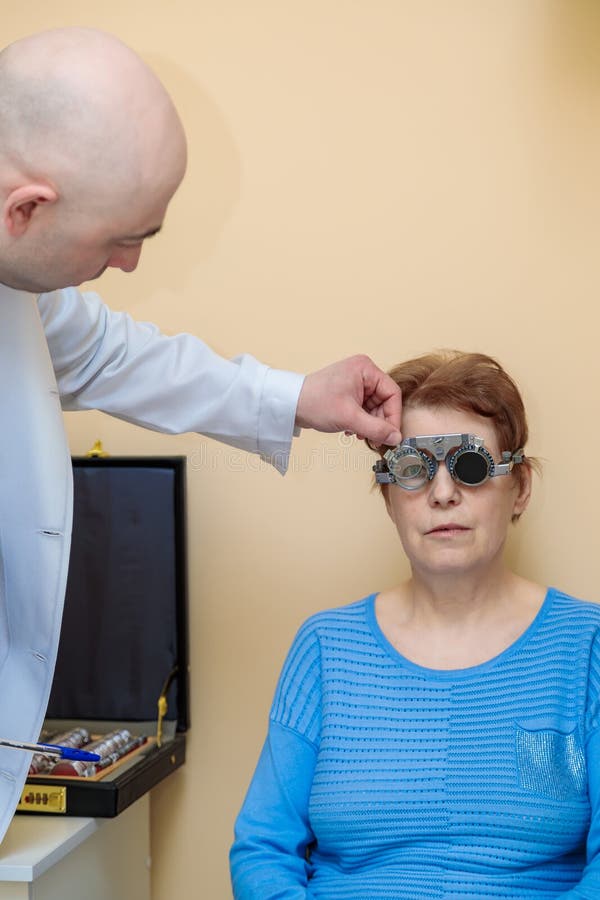 Un optometrista maschio controlla la vista di una donna adulta con una cornice di prova fotografia stock libera da diritti