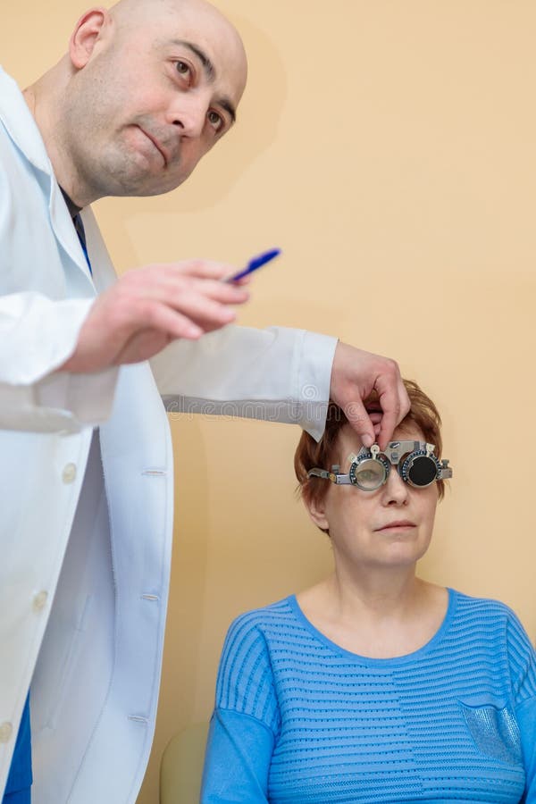 Un optometrista maschio controlla la vista di una donna adulta con una cornice di prova fotografia stock