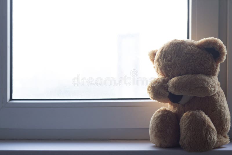 A soft toy bear cries sitting on a windowsill. There are noises in the photo, because the photo is dark. A soft toy bear cries sitting on a windowsill. There are noises in the photo, because the photo is dark